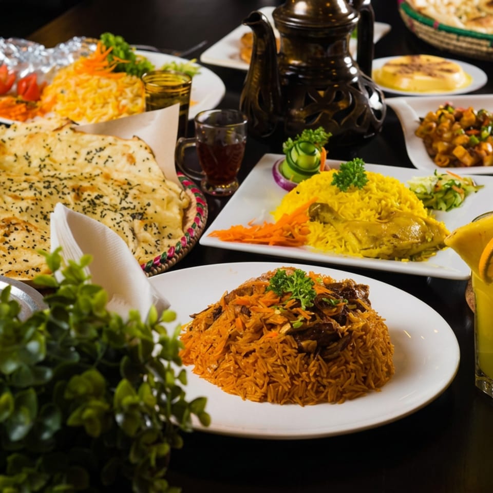 Assorted Indian dishes including biryani, naan, curry, rice, vegetables, tea, and a lemon drink arranged on a restaurant table.